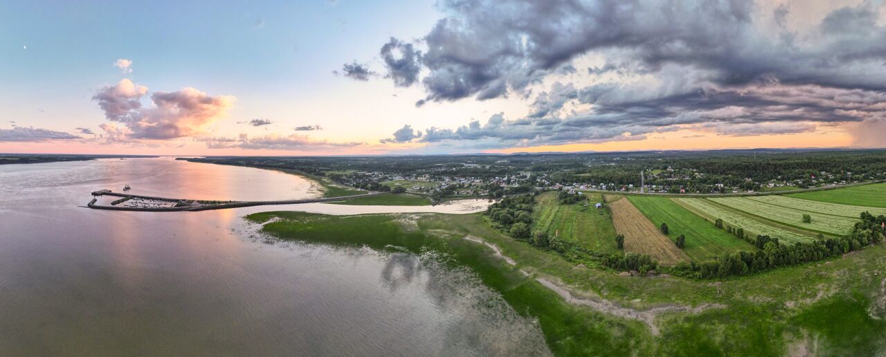 Vue aérienne au coucher du soleil sur le fleuve, une marina et des champs cultivés.